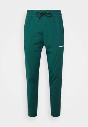 Groene sportbroek met een elastische tailleband en trekkoord. Voorzien van een zijzak en een witte "PEGADA"-logo langs het been. Glad oppervlak.