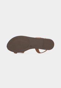 Η σόλα του σανδάλιου κοιτάζει προς τα πάνω, δείχνοντας τον επίπεδο καφέ καουτσούκ πάτο με υφή για καλύτερη πρόσφυση και λεπτά ανοιχτόχρωμα δερμάτινα λουράκια που είναι μερικώς ορατά.