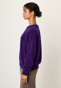 Maglione viola morbido con scollo rotondo, spalle scese e polsini a costine. Ha una vestibilità ampia e una texture morbida.