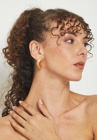 Zlaté náušnice v tvare polmesiaca s hladkým, lešteným povrchom, nosené na ušnom lalôčku, na neutrálnom pozadí.