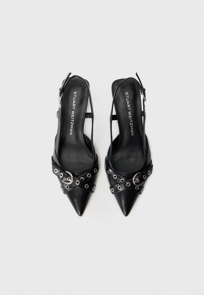 Mustat, kärjellinen slingback-korkokengät, joissa on hopeiset reikäsoljettinauhat ja "Stuart Weitzman" -painetut pohjat valkoisella taustalla.