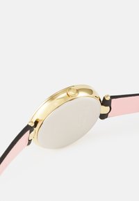 Reloj redondo con caja de acero inoxidable dorado, fondo plateado y correa bicolor de cuero negro y rosa. Presenta una corona lateral.