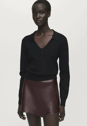 Black knit pullover with a V-neck and long sleeves, paired with a dark burgundy faux leather wrap skirt. Smooth textures and clean lines.