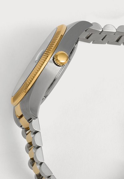 Vue latérale d'une montre-bracelet de luxe avec une lunette en or, une couronne en or, et un bracelet en métal bicolore argent et or.