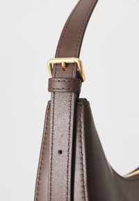 Tracolla di una borsa in pelle marrone con dettagli in metallo dorato, caratterizzata da una superficie liscia e cuciture visibili lungo i lati.