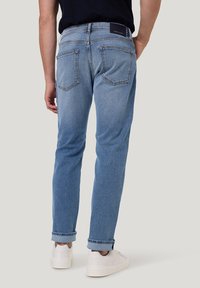 Jeans en denim bleu clair avec une coupe ajustée, dotés de deux poches arrière et de poignets retroussés, assortis à des baskets blanches.