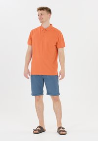 Kortärmad orange polo, blå shorts, bruna sandaler. Slät tyg, krage med knappar, avslappnad passform, upprullade shorts.