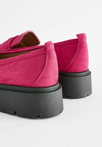 Pantofi din suede roz cu o talpă groasă neagră. Prezintă un vârf rotunjit și detalii cusute pe partea superioară. Fără elemente metalice vizibile.