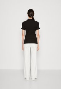 Polo shirt nero a maniche corte con un design aderente, abbinato a pantaloni bianchi a gamba larga, vista da dietro. Stile minimalista.
