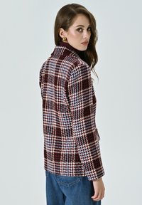 Blazer en mélange de laine avec un motif pied-de-poule multicolore dans des tons bordeaux, bleu et crème. Col cranté et fermeture à un bouton.
