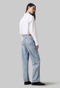 Camisa blanca corta con botones combinada con jeans rectos azul claros, que cuentan con un diseño clásico de bolsillo y calzado negro.