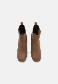 Botas de tobillo marrones de ante con una textura suave, que presentan un diseño minimalista y un tacón bajo, con parte superior abierta y acentos laterales.