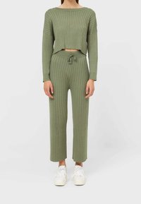 Olijfgroene co-ord set gemaakt van ribbelstof; bevat een cropped top met lange mouwen en broek met drawstring en wijde pijpen voor een comfortabele pasvorm.