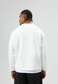 Witte sweater met lange mouwen, losse pasvorm, ronde hals en een gladde textuur, gecombineerd met een wit shirt en zwarte broek.