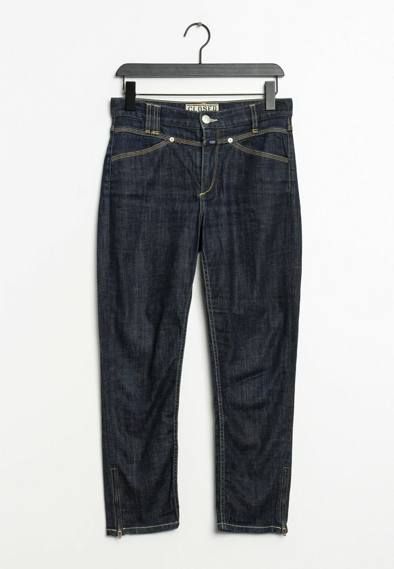 Jean en denim bleu foncé avec coutures jaunes suspendu sur un cintre noir sur fond blanc, avec poches avant et fermetures éclair aux chevilles.