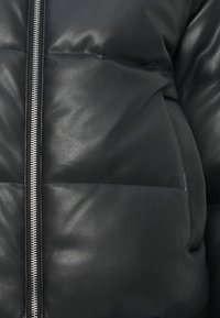 Černá umělá kožená péřová bunda s prošívanou strukturou, stříbrným zipem a horizontálním šitím. Materiál vypadá měkce a mírně leskle.