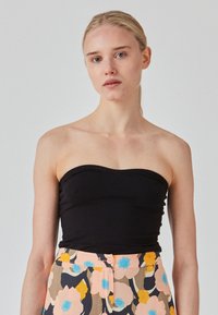 Top negro sin tirantes con un diseño ajustado. Combinado con pantalones con patrón floral que presentan acentos en rosa, azul y amarillo. Textura suave.