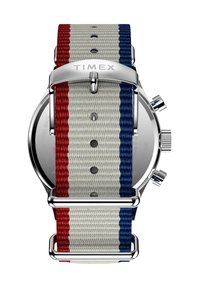 El reloj Timex cuenta con una caja de acero inoxidable plateada, una correa de lona gris con rayas rojas y azules, y una hebilla pulida con el logo.
