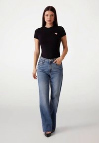 T-shirt noir ajusté avec un petit logo, associé à un jean droit bleu clair taille haute et des escarpins noirs à bout pointu.