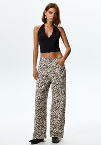 Top corto nero con dettaglio arricciato abbinato a pantaloni larghi con stampa leopardata in beige e marrone, indossato con calzature nere.