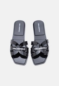 Μαύρα σανδάλια slide από δέρμα με λουστρίνι Karl Lagerfeld με λουριά σε σχήμα σταυρού και τετράγωνη σχεδίαση μύτης σε λευκό φόντο.