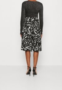 Top negro de manga larga con una textura brillante, combinado con una falda hasta la rodilla con un estampado floral en blanco y negro y zapatos de tacón alto negros.