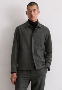 Szara koszula marynarkowa w prążki z kołnierzem, przednią kieszenią i zapięciem na guziki, wykonana z teksturowanej tkaniny, zestawiona z czarnym golfem.