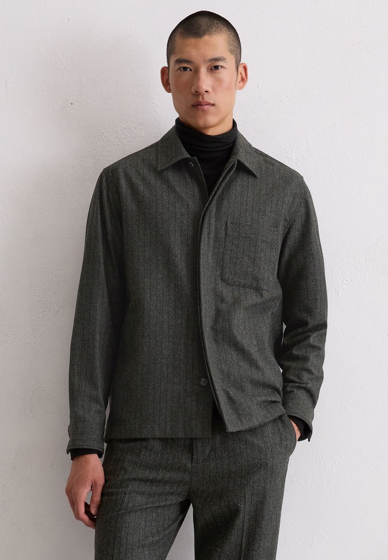 Szara koszula marynarkowa w prążki z kołnierzem, przednią kieszenią i zapięciem na guziki, wykonana z teksturowanej tkaniny, zestawiona z czarnym golfem.