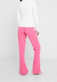 Pantaloni rosa a gamba larga realizzati in tessuto morbido, caratterizzati da una vita alta e una silhouette pulita. Abbinati a un top bianco a coste.