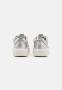 Silver waterproof sneakers with a textured rubber sole, featuring a pull tab and minimalist design. Rear view shows iconic brand logo.