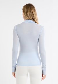 Camicia a maniche lunghe color azzurro chiaro realizzata in tessuto morbido con design aderente. Presenta un colletto classico e una finitura leggermente strutturata.