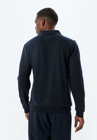 Marineblaues langärmliges Polohemd aus strukturiertem Stoff, mit klassischem Kragen und gerippten Bündchen, Rückansicht schlicht.