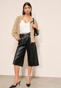 Šviesiai ruda bombers tipo striukė vilkima ant baltos, nėriniuotėmis apipintas kamizolos, derinama su juodomis dirbtinio kailio culottes kelnėmis ir juodais smailiais bateliais. Pridedamas juodas rankinės.