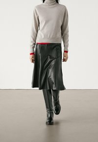 Grauer Rollkragenpullover mit rotem Akzent am Saum, kombiniert mit einem schwarzen Lederminirock, glatte Textur, knielang, getragen mit schwarzen Stiefeletten.