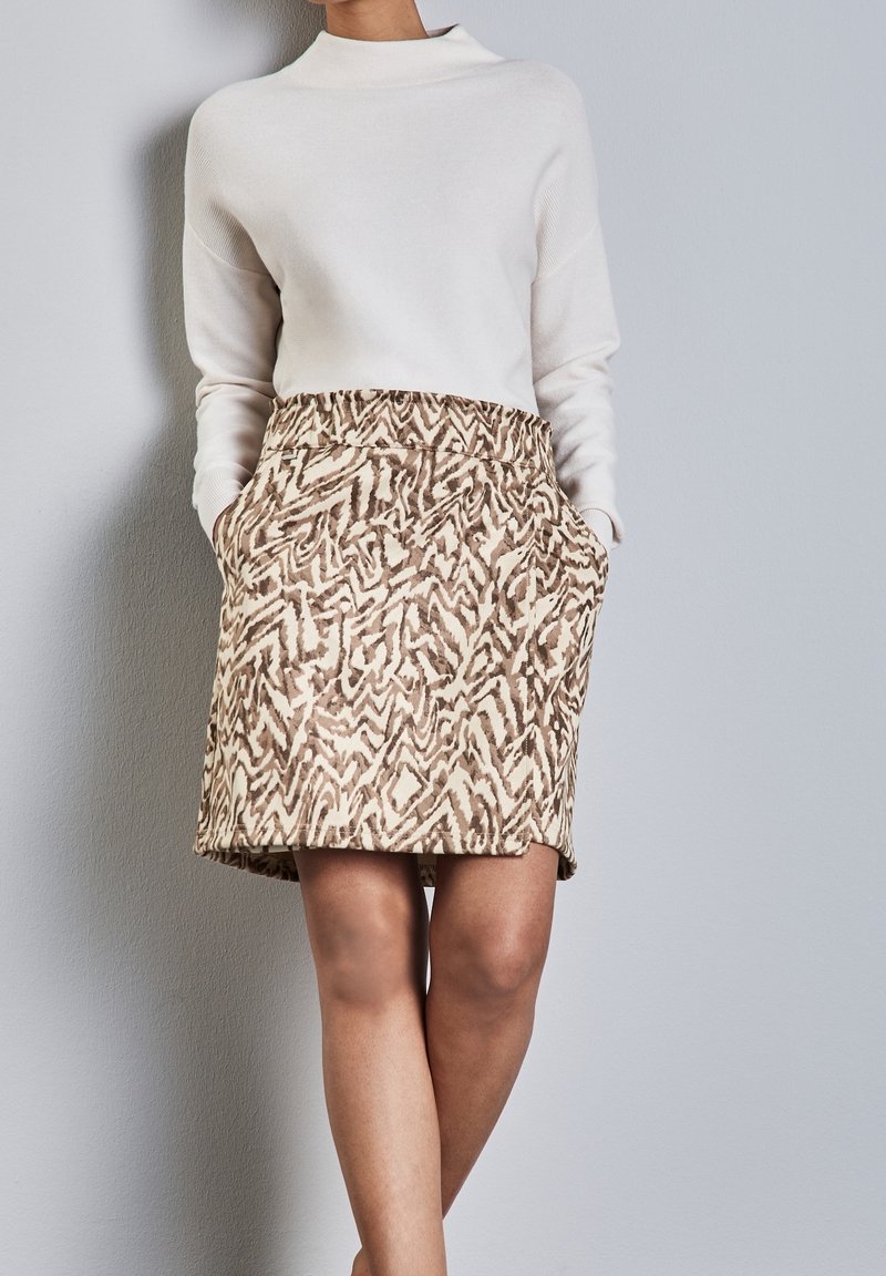 Haut ample crème associé à une jupe beige jusqu'aux genoux avec un motif abstrait marron et des poches latérales.