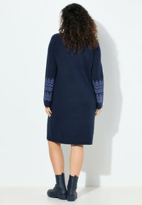 Abito in maglia color blu navy scuro con maniche lunghe, caratterizzato da un motivo geometrico azzurro sui polsini. Tessuto liscio, taglio al ginocchio, vestibilità dritta.