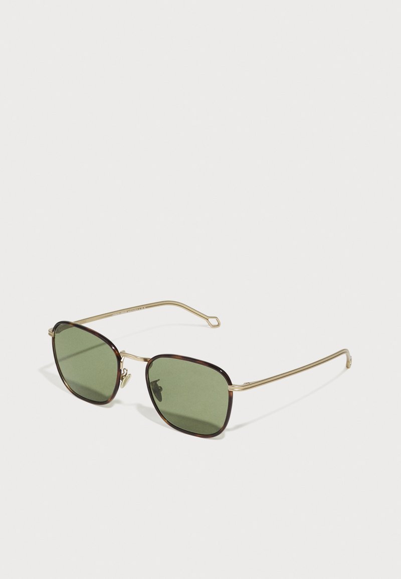 Sunglasevi sa kvadratnim oblikom leća, tamnozeleni nijansirani leće, i zlatni metalni okvir s smešnim naglascima. Imaju tanke ručke.