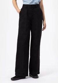 Svarta vida byxor i ett slätt, robust tyg, med hög midja och sidofickor, bärs med svarta skor.