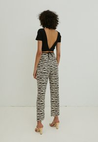 Schwarzes Crop-Top mit tiefem V-Rücken, kombiniert mit hochgeschnittenen cremefarbenen Hosen mit schwarzem Wellenmuster, ergänzt durch beige Absätze.