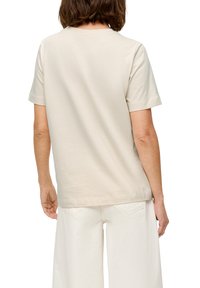 Beige Baumwoll-T-Shirt mit kurzen Ärmeln und rundem Ausschnitt, von hinten gezeigt. Hat eine glatte Textur und eine lässige Passform.