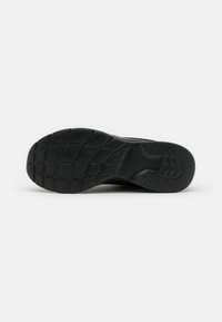 Suela de zapato deportivo negro con una superficie de goma texturizada, que presenta un patrón de huella geométrica para mayor agarre y un diseño ligero.