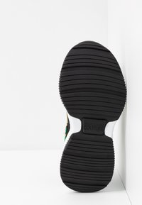 Semelle en caoutchouc noir avec rainures texturées ; dotée d'accents colorés, d'un écusson logo et d'une section talon blanche. Conçue comme une basket.