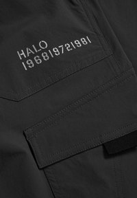 Zwarte stof met een gladde textuur heeft een rechthoekige zak. De bedrukte tekst "HALO 196819721981" is zichtbaar in een contrasterende kleur.