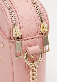 Borsa a mano in pelle rosa con superficie texturizzata, doppi zip metallici, dettagli in oro e attacco a catena per la tracolla.