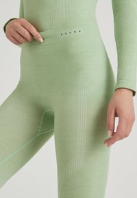 Light green thermal leggings with ribbed texture, featuring a logo waistband and contrasting seams. Includes a discreet opening detail.