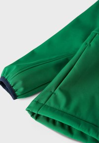 Grön jacka av tyg med slät yta, med elastiska muddar i marinblått. Designen inkluderar sömnadsdetaljer och en strukturerad form.