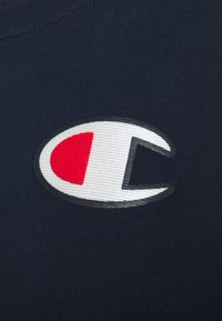 Marinblått tyg med en framträdande broderad logotyp som har en röd halvcirkel och ett vitt bokstav 'C' inramat i svart.