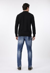 Μαύρο πλεκτό πουλόβερ με στρογγυλή λαιμόκοψη, συνδυασμένο με μπλε τζιν παντελόνι με φθορές και μαύρα αθλητικά παπούτσια με λευκές ρίγες.