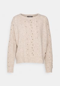 Beige gebreide trui met een losse pasvorm, voorzien van decoratieve gouden studs, een ronde halslijn en gestructureerde stikpatronen aan de voorkant.