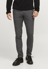 Grau gemusterte, texturierte Hose mit schmalem Schnitt und mittelhohem Bund, kombiniert mit schwarzen Schnürschuhen.